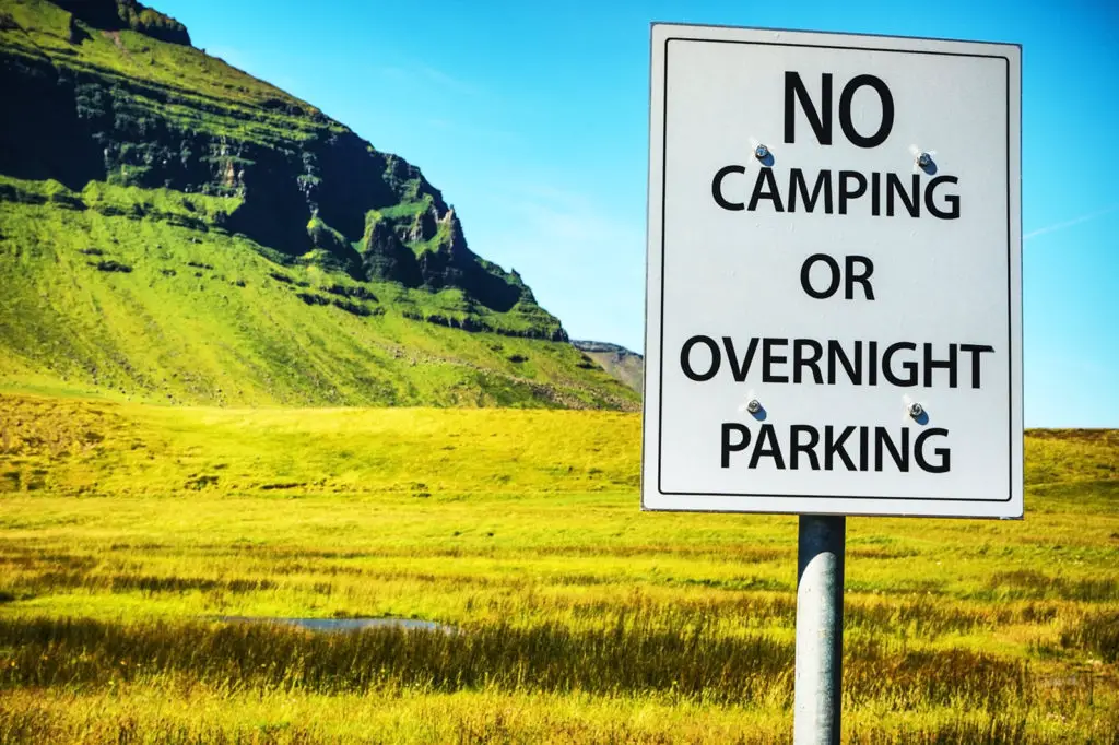 Image with mountain in background and sign in foreground saying "No Camping of Overnight Parking"