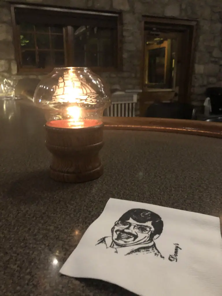 Image of candle and cocktail napkin with Donny's face from Donny's Glidden Lodge on it