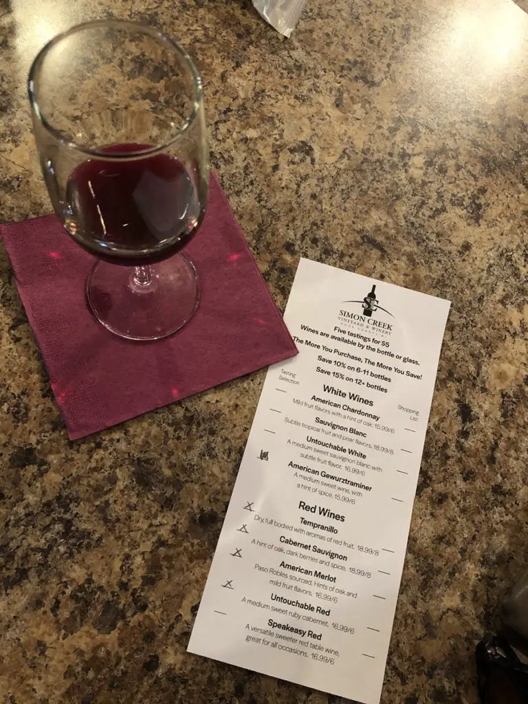 Image of wine glass on napkin with red wine in it. Along side it a wine tasting menu