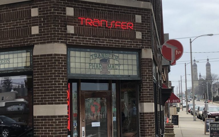 Image of outside of Transfer Pizza restaurant in Milwaukee WI. Brick corner building with red neon sign reading Transfer above door