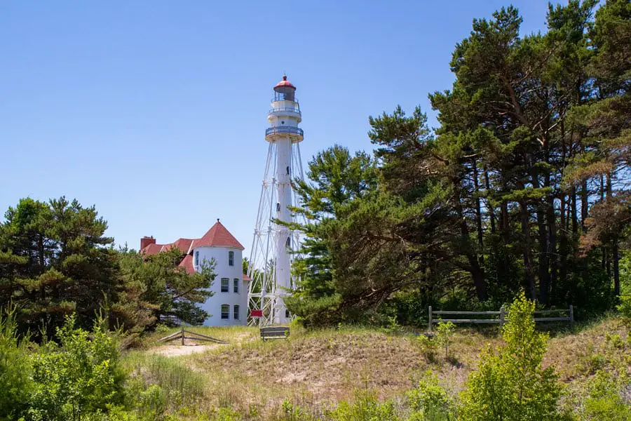 Image of Rawley Point Lighthouse. Lighthouse is white with a building to the side of it. 