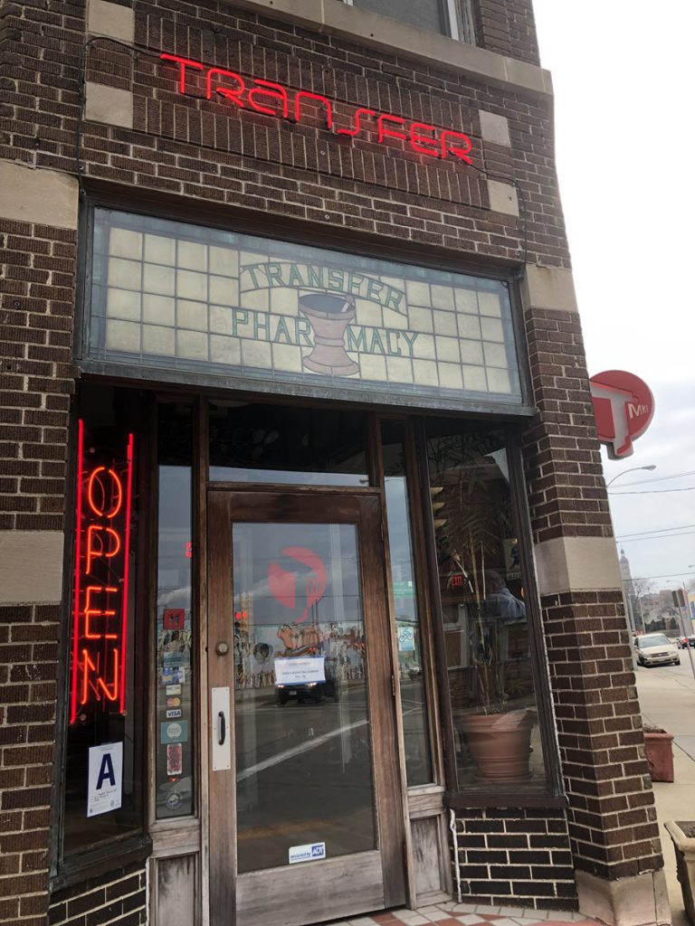 Image of the outside of Transfer Pizza. A red brick building with a red neon Transfer Pizza sign