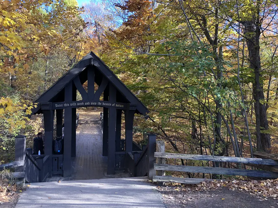 Image of wooden structure at the entrance of Seven Bridges Park in South Milwaukee, WI. Surrounding trees are turning colors for fall. 