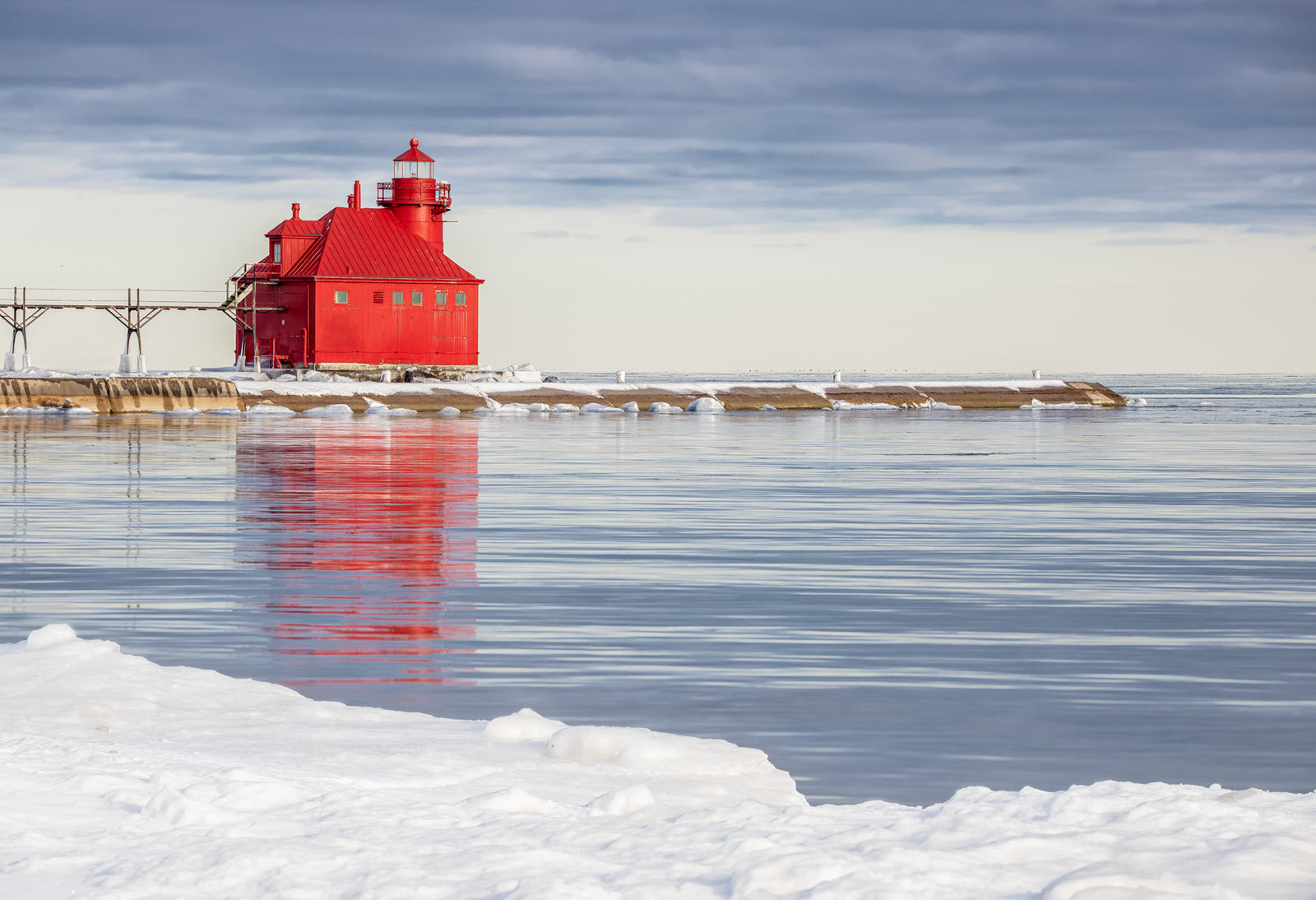 Image of red lighthouse in Sturgeon Bay, Wisconsin in Winter. Red Lighthouse is in the distance with a snow covered shoreline in the foreground.