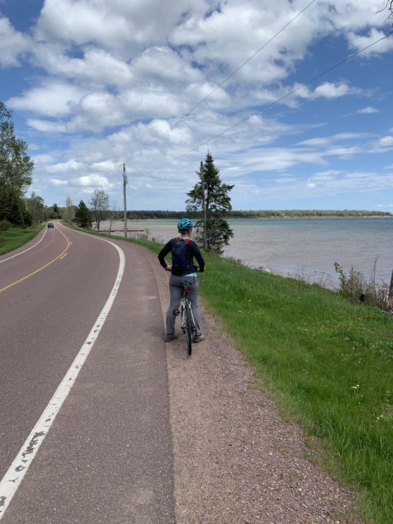 A picture of a biker stopped on the side of the road on Madeline Island overlooking Lake Superior. 