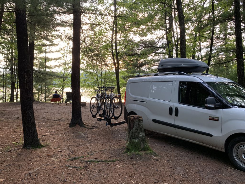 Image of small white campervan with two bikes on the back. Two camp chairs in the distance with campers looking out at the Chippewa River in Wisconsin