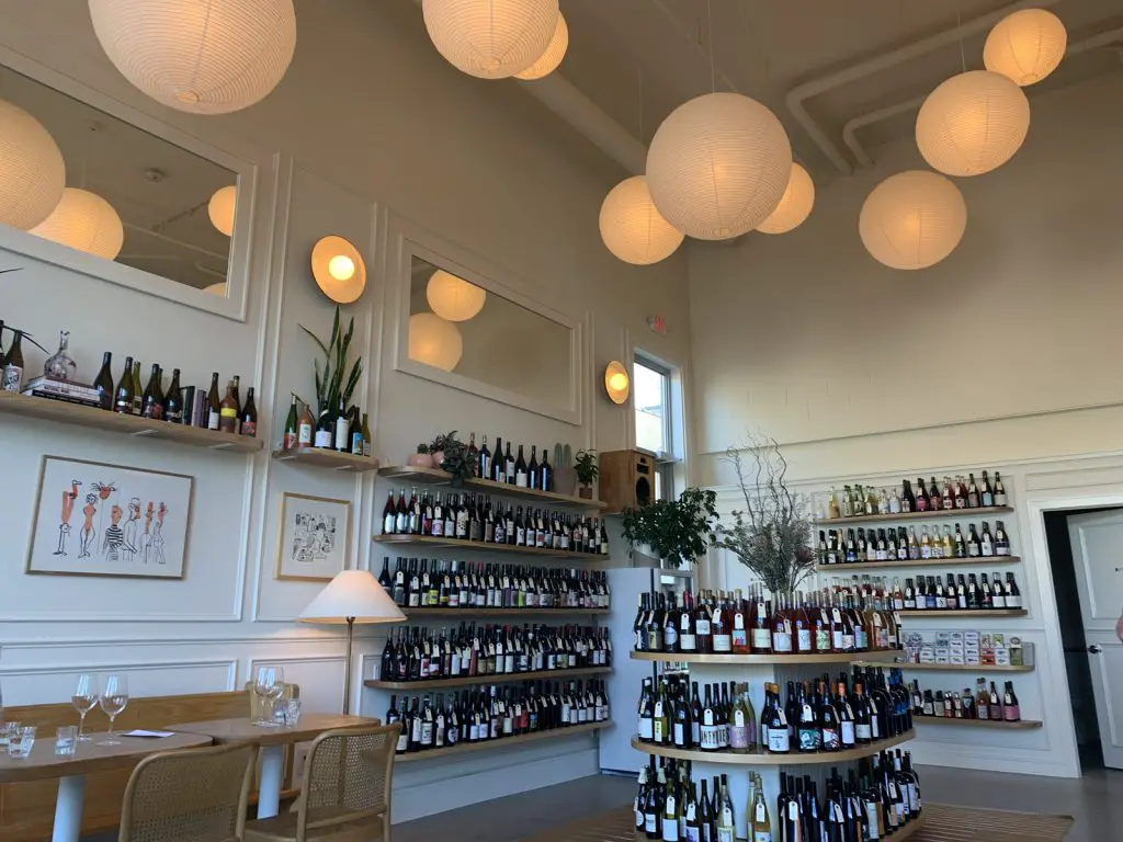 Image of inside of Nonfiction Natural Wine in the Bay View Neighborhood in Milwaukee WI. Wine bottles for sale along wall and off-white circle lights illuminate the room