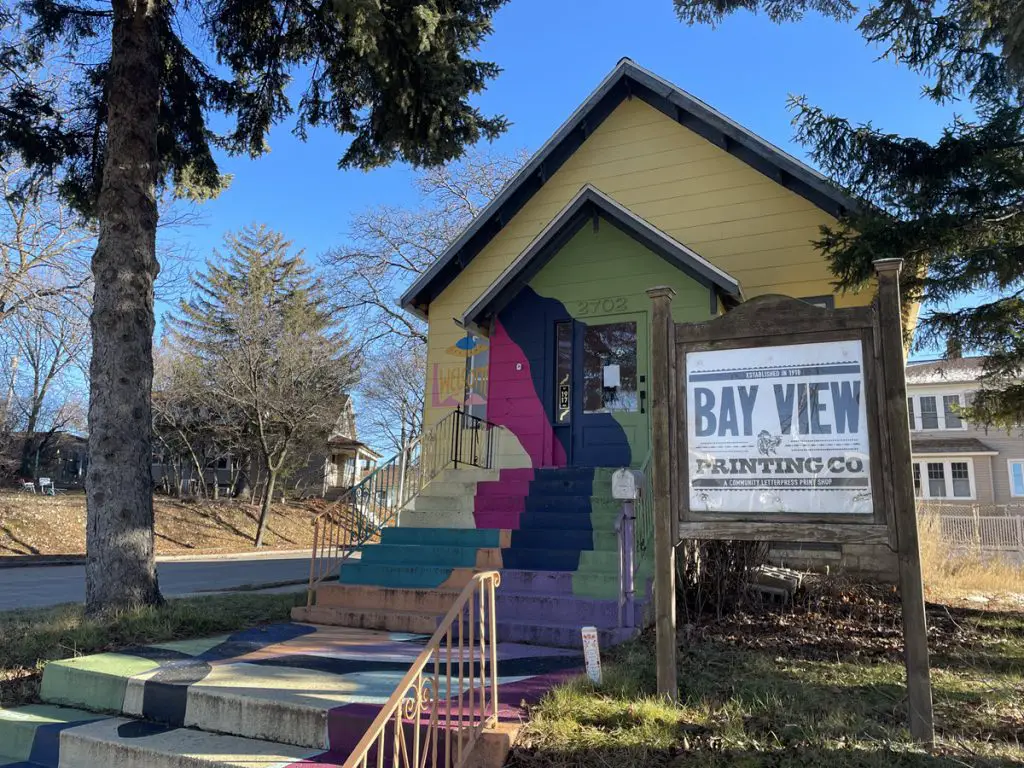 Image of the front of Bay View Printing Co in Milwaukee WI. Building is painted in bright colors; yellow, pink, purple, green